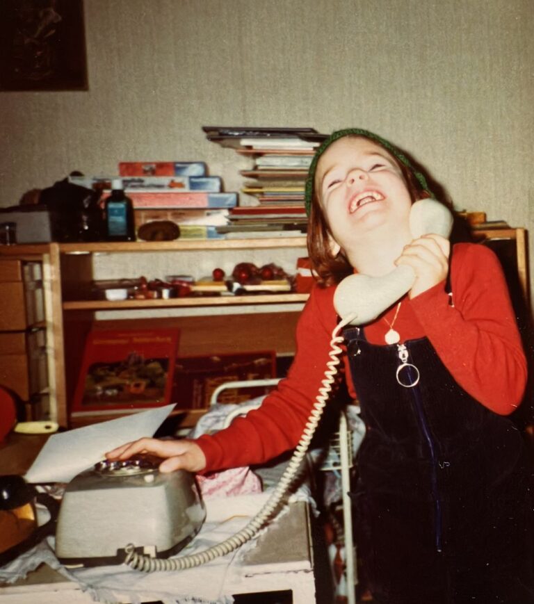 Marie-Gabriele Massa als Kind lachend mit einem Schnurtelefon – Ausdruck von Humor und Leichtigkeit